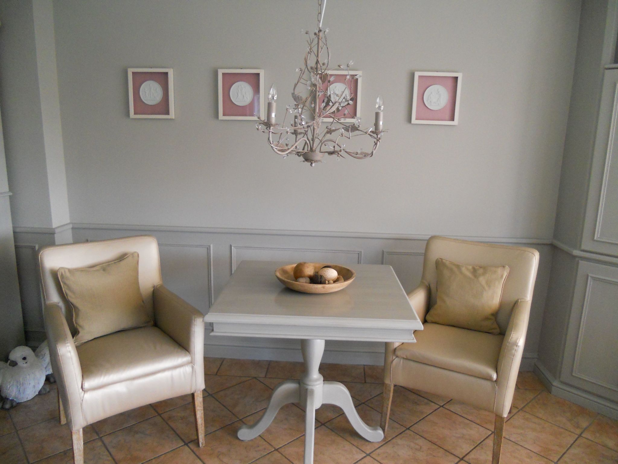 Un coin repas comprenant deux fauteuils en cuir beige, une table blanche et un lustre.
