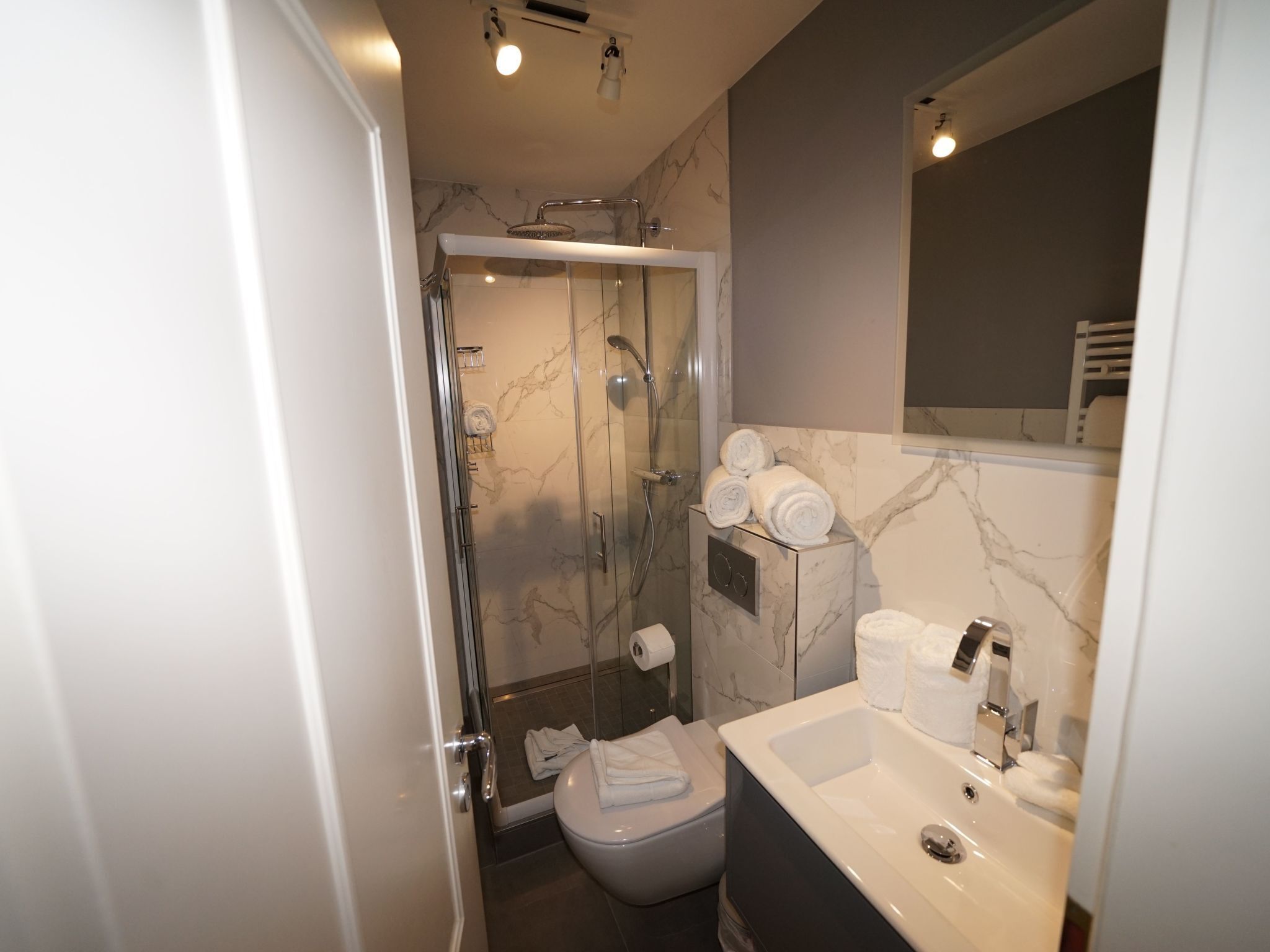 Een moderne badkamer met een douchecabine van glas, een toilet en een wastafel met spiegel.