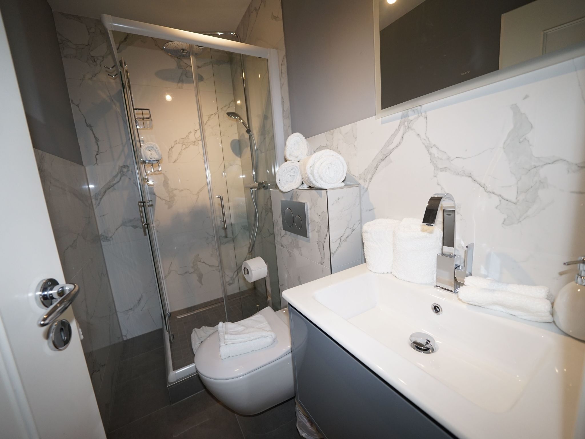 A modern bathroom with a glass-enclosed shower, a white sink, and marble walls.
