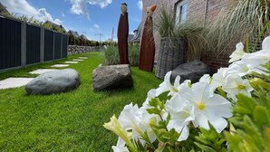 Ein gepflegter Garten mit einem Ziegelhaus, großen Steinen und weißen Blüten.