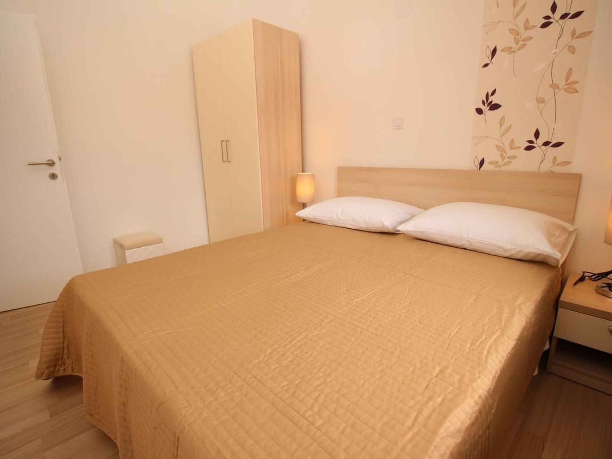A bedroom with a bed, bedside table, nightstand, wardrobe, and a wall with a leaf pattern.