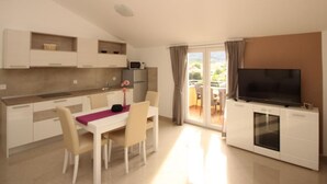 A modern kitchen with white cabinets, a dining table with chairs, a TV on a cabinet, and a sliding glass door leading to an outdoor area. - Gorica II A2+2 br.8 by Interhome (Krk/Baška)