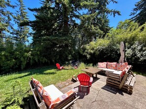 Une terrasse extérieure avec un fauteuil Adirondack rouge, un banc en bois et un espace salon agrémenté de coussins.