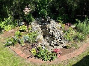 Un jardin agrémenté d’une petite cascade, de différentes plantes et d’un sentier en briques.
