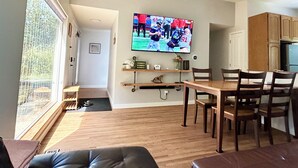 A living room with a TV, wooden furniture, and a view through a window. - Cascading Stream Oasis: 4BR Near SeaTac Airport with Air Conditioning (Burien)