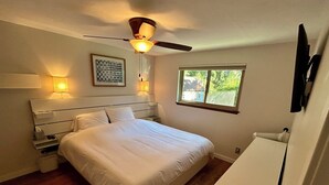 Un dormitorio con una cama, lámparas de noche, ventilador de techo, una ventana y un televisor montado en la pared.