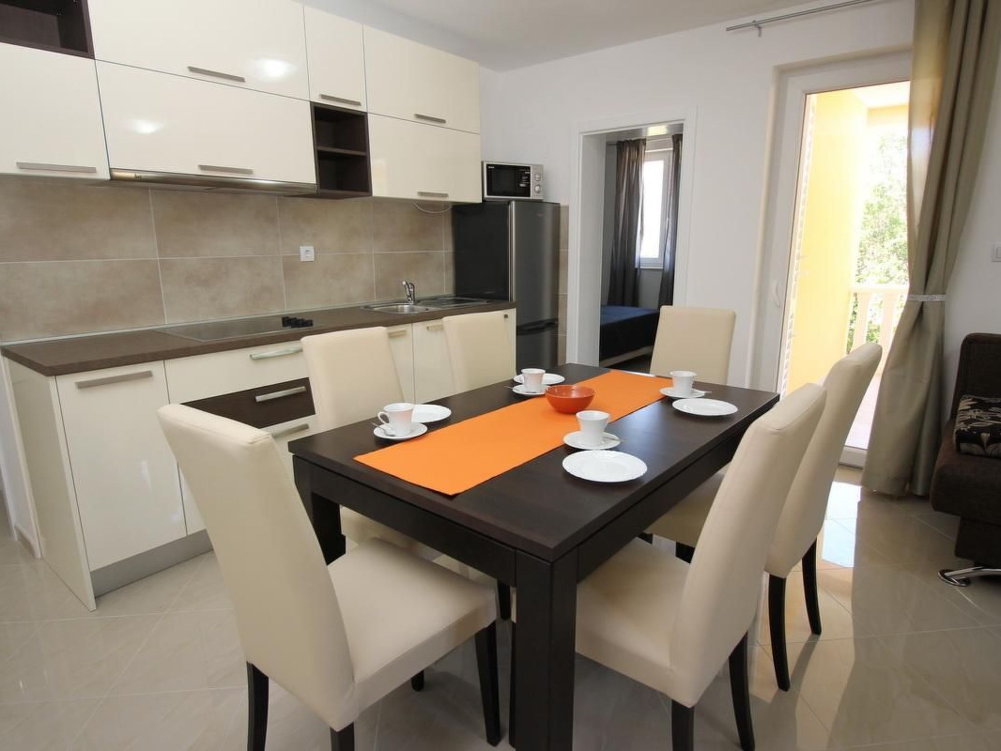 A modern kitchen with white cabinets, a dark countertop, and a dining area with a table set for four.