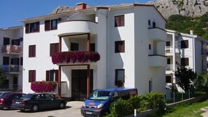 A multi-story building with balconies, a car parked in front, and a mountainous backdrop. - Grozdana Nr.1A by Interhome (Krk/Baška)