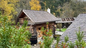 Une cabane rustique au toit en pente, entourée d’une zone boisée aux couleurs automnales.