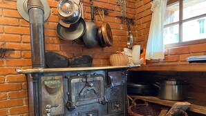 Une cuisine rustique avec un mur en briques, un poêle, des casseroles suspendues et un panier en osier.
