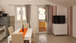 A modern kitchen with a microwave, a dining table with chairs, a TV on a stand, and a sliding glass door leading to an outdoor area. - Gorica II A2+1 br.9 by Interhome (Krk/Baška)