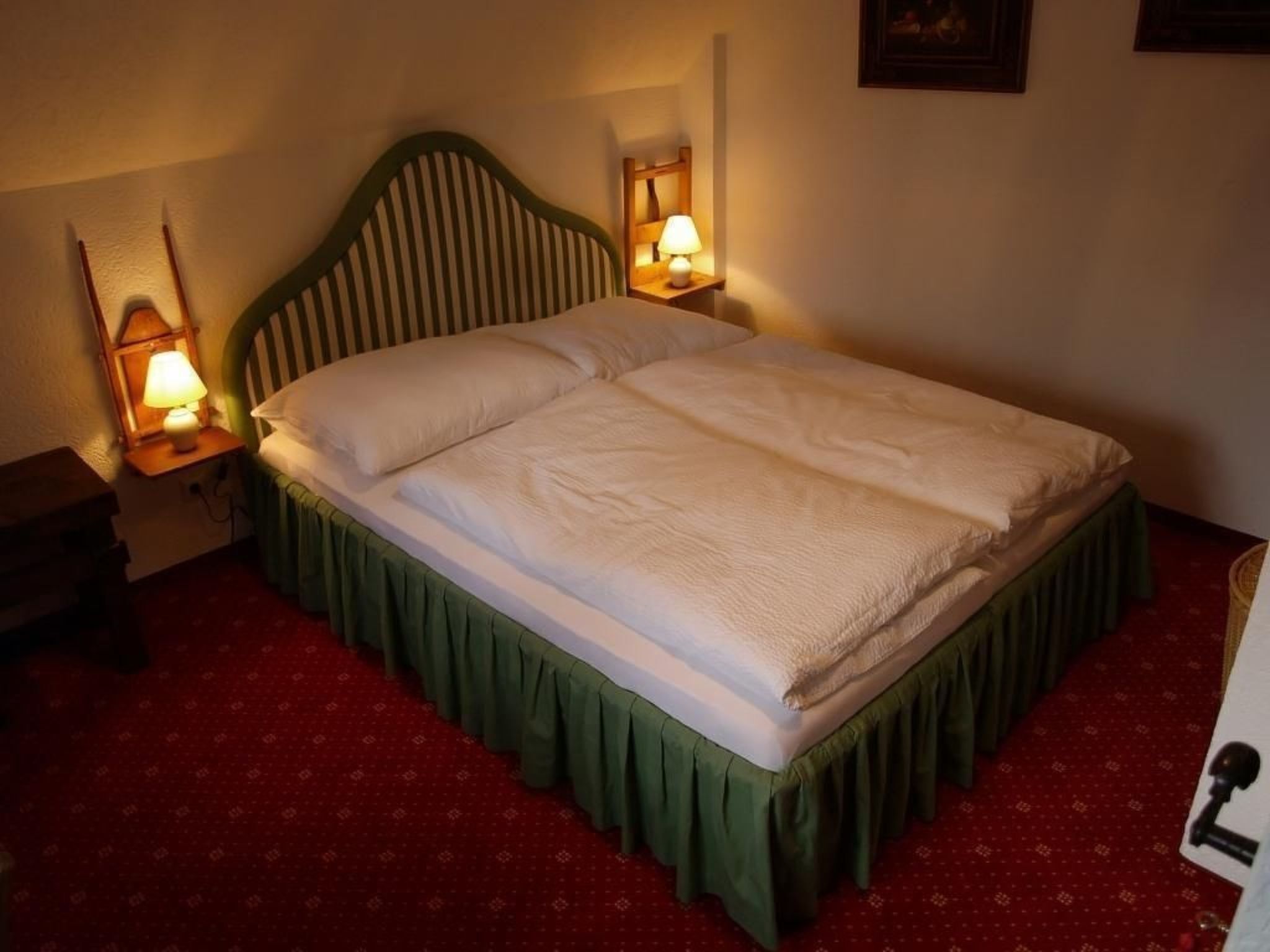 Una cama con falda verde, dos lámparas de noche y una alfombra roja.