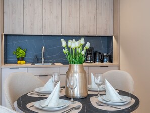 A modern dining area with a round table set for four, featuring white napkins, clear wine glasses, and a vase with white tulips. - in den Sun Towers am Meer by Interhome (Swinoujscie)