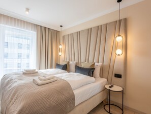 A modern hotel room with a large bed, a bedside table, and a view of the city through sheer curtains. - in den Sun Towers am Meer by Interhome (Swinoujscie)