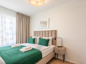 A modern hotel room with a bed, green and white bedding, a bedside table with a lamp, and a window with sheer curtains. - Gemütliche, helle Ferienwohnung an der Ostsee by Interhome (Swinoujscie)