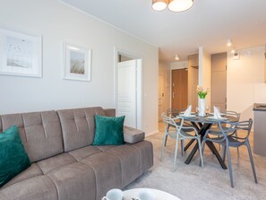 A modern living room with a grey sofa, a dining table set for four, and a kitchen area visible in the background. - Gemütliche, helle Ferienwohnung an der Ostsee by Interhome (Swinoujscie)