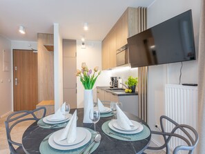 A modern kitchen with a flat-screen TV, a dining area with a round table set for four, and a vase with flowers. - Gemütliche, helle Ferienwohnung an der Ostsee by Interhome (Swinoujscie)
