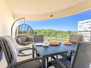 Un balcone con mobili in vimini, una poltrona amaca e un tavolo apparecchiato per la colazione.
