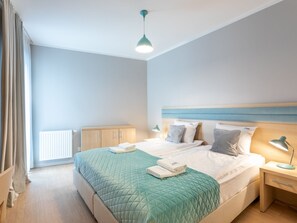 Ein modernes Schlafzimmer mit Bett, Nachttischen, Heizkörper und einem fenster mit Vorhängen.