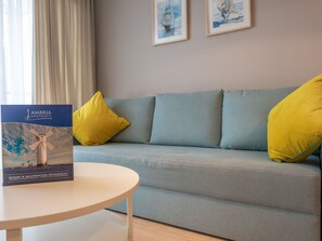 En lyseblå sofa med to gule puder, et lille rundt bord med en brochure, og to billeder hænger på væggen.