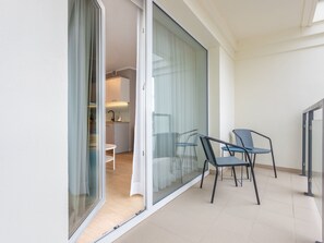 Ein Balkon mit einer Schiebetür, einem kleinen Tisch, zwei Stühlen und einem Blick auf eine Küchenzeile durch die Tür.