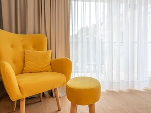 Ein gelbes Sofa mit Holzbeinen und ein passendes Ottomanen in einem Raum mit transparenten Vorhängen und Holzboden.