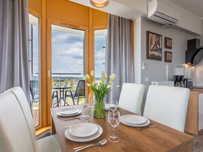 A dining area with a wooden table set for four, a vase of white flowers, and a view of a cityscape through large windows. - Tower 97 in hervorragender Lage by Interhome (Swinoujscie)