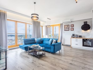 A modern living room with a blue sofa, a glass coffee table, and a view of the city through large windows. - Tower 97 in hervorragender Lage by Interhome (Swinoujscie)