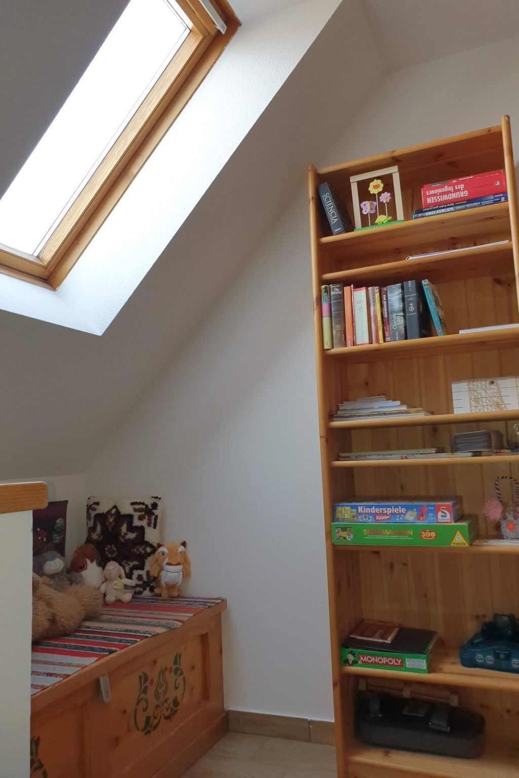 Une pièce avec un plafond en pente, une lucarne, une bibliothèque en bois et un espace de jeux avec des jouets et un tapis à rayures.