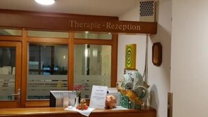 Ein Empfangstisch mit einem Schild, das 'Therapie-Rezeption' zeigt, und einer kleinen Statue auf der Theke.