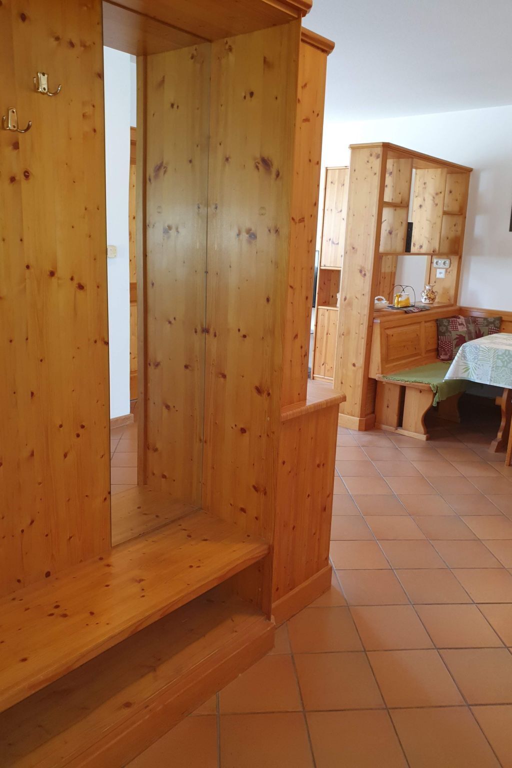 A wooden interior with a bench and a table, a tiled floor, and a wooden cabinet.