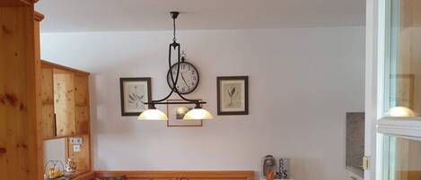 A cozy room with a wooden bench, a table with chairs, a wall clock, and a ceiling light fixture.
