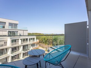 A balcony with two round tables and two blue chairs, overlooking a modern building and a forested area. - Topmoderne Ferienwohnung Albus 419 by Interhome (Swinoujscie)