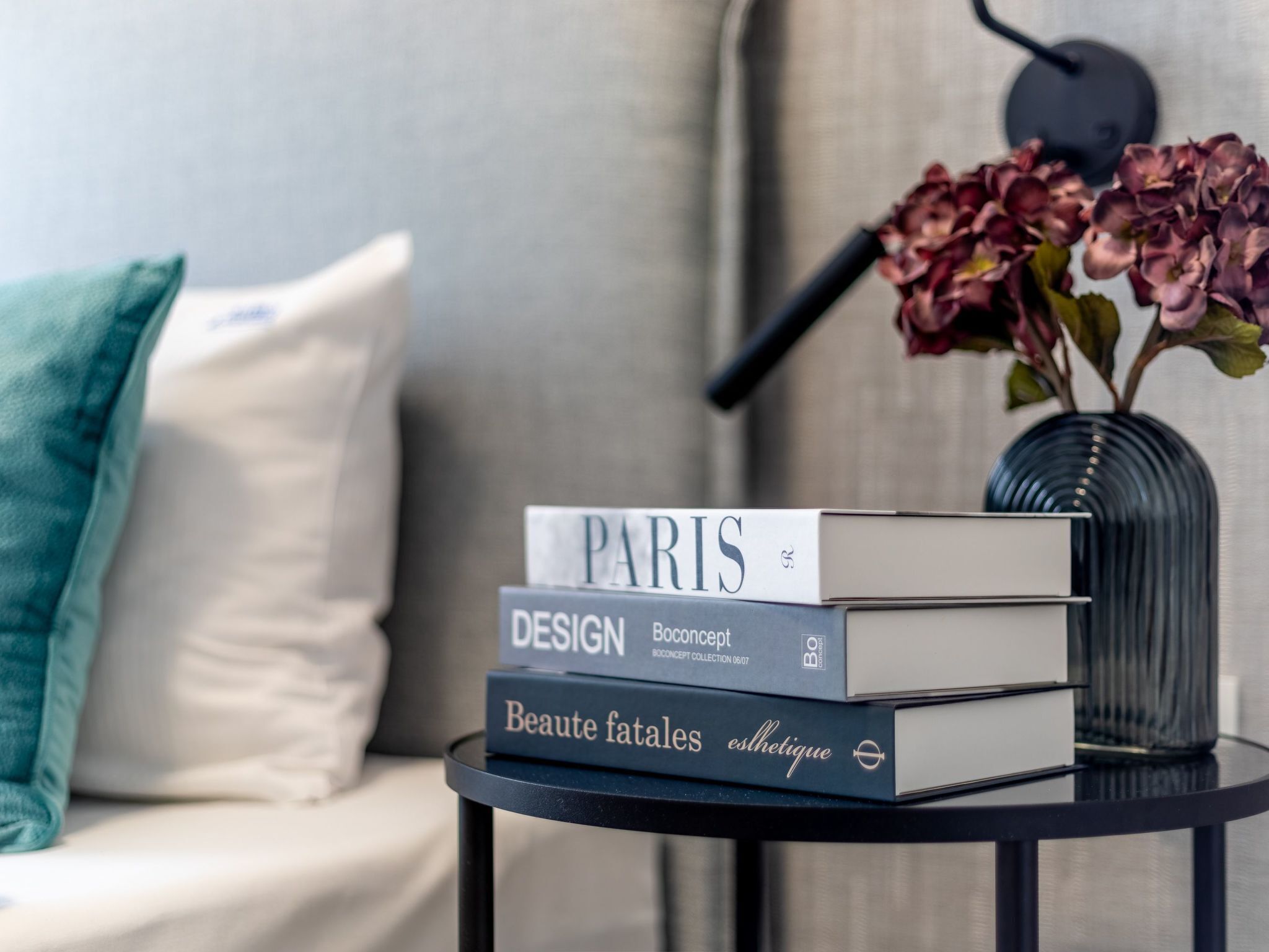 A stack of books on a small round table with a vase of flowers in the background.