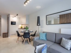 A modern living room with a grey sofa, a dining table with chairs, and a kitchen area in the background. - Elegante Ferienwohnung an der Ostsee by Interhome (Swinoujscie)