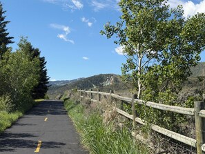 A paved road with a wooden fence on one side and trees on the other, leading towards a hilly landscape. - Cozy 2-bedroom condo with Fireplace in a perfect Park City location/Olympic Park (Park City)