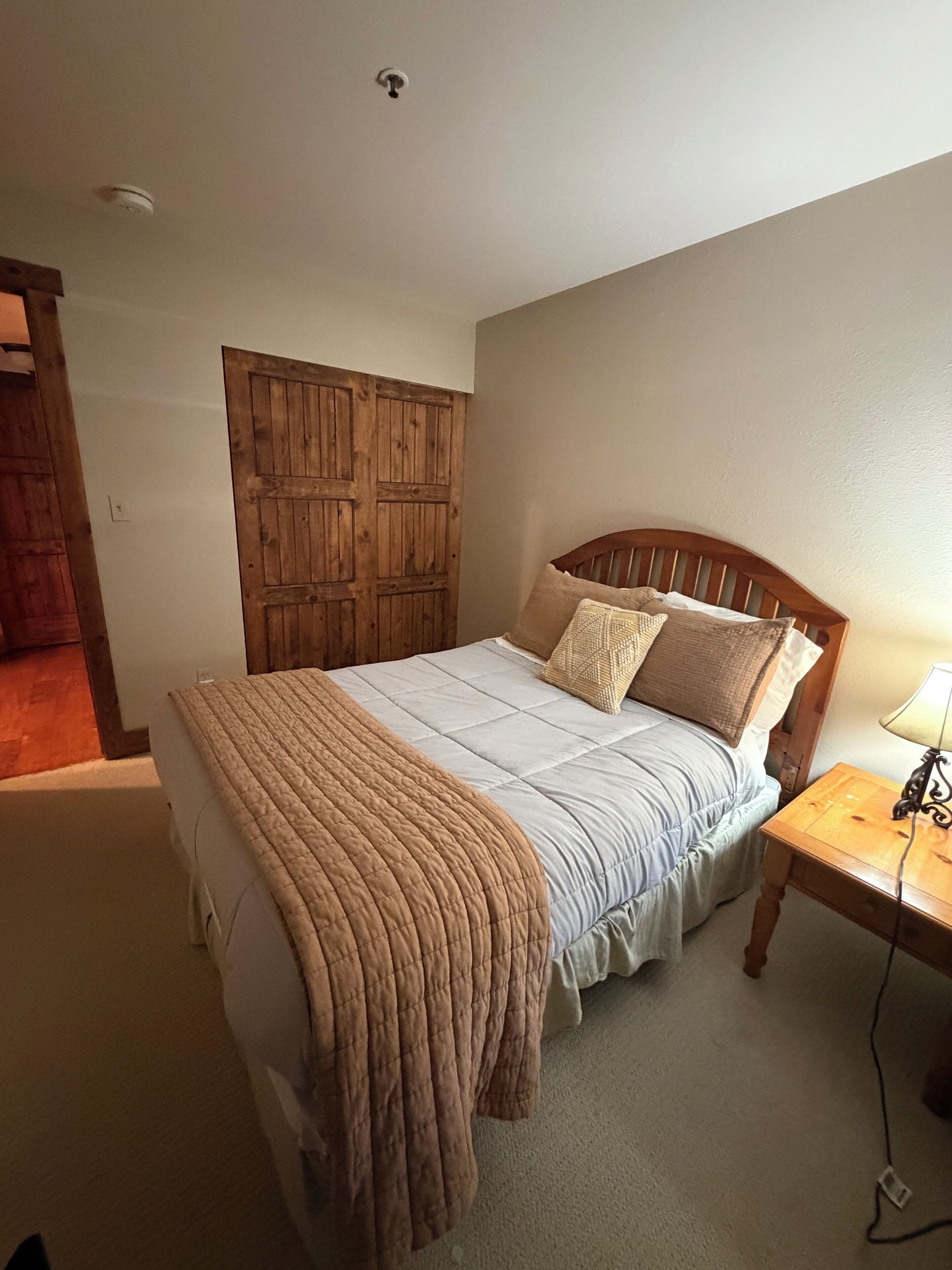 Un dormitorio con cama, armario de madera, mesita de noche y lámpara.