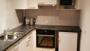 A compact kitchen with white cabinets, a stainless steel microwave, a built-in oven, and a small refrigerator. - Graz Green Studio by Interhome (Graz)