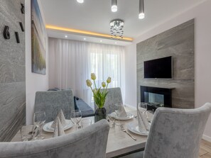 A modern dining area with a table set for four, a sofa, a fireplace, and a TV mounted on the wall. - Ostsee-Ferienwohnung Bianco 8 mit Kamin by Interhome (Swinoujscie)