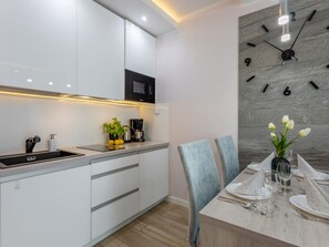 A modern kitchen with white cabinets, a black microwave, and a coffee maker. There is a dining table set with plates, glasses, and a vase of flowers. - Ostsee-Ferienwohnung Bianco 8 mit Kamin by Interhome (Swinoujscie)