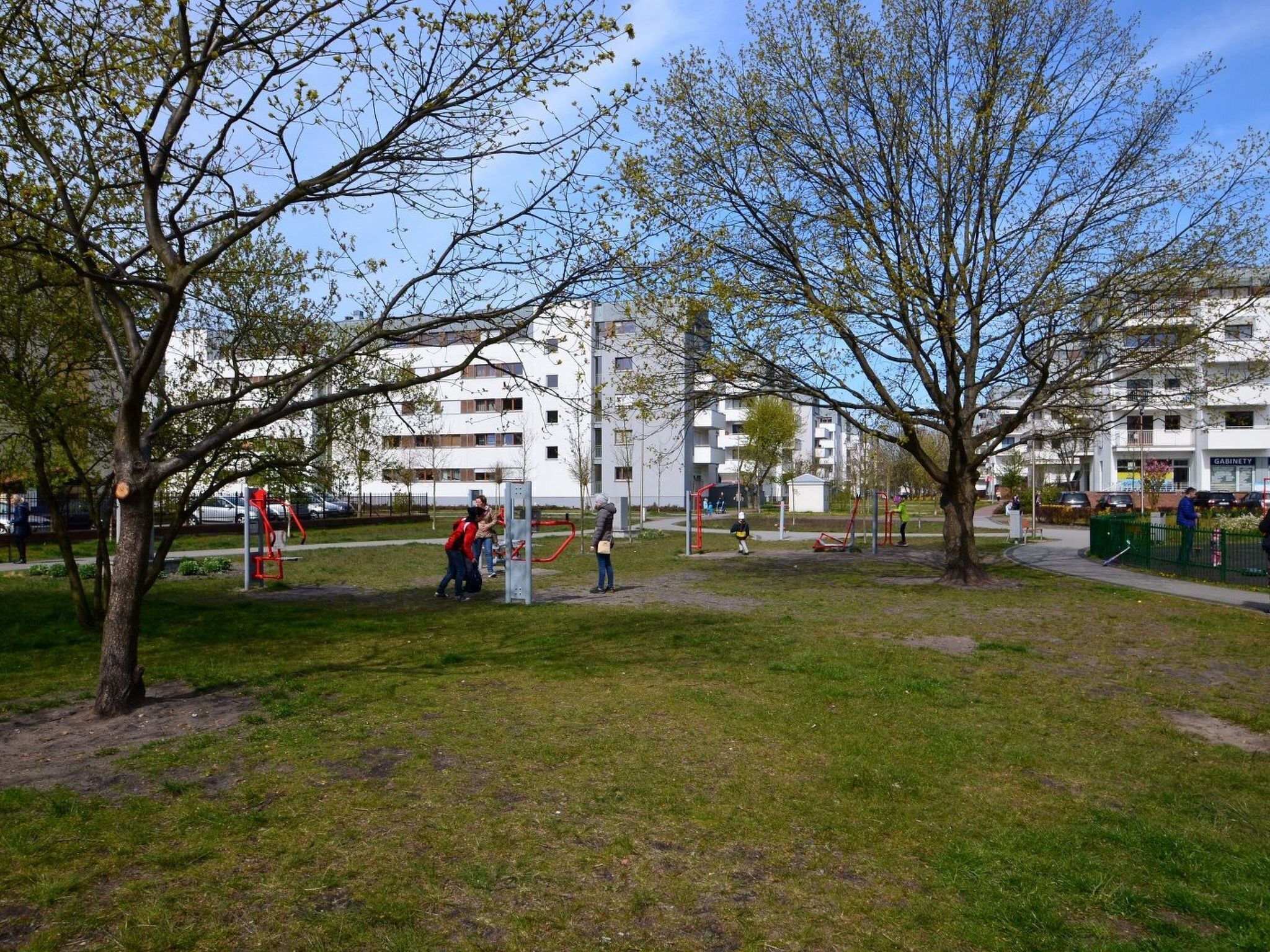 A park with exercise equipment, trees, and residential buildings in the background.
