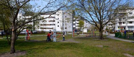 A park with exercise equipment, trees, and residential buildings in the background.