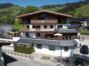 Ein zweistöckiges Gebäude mit Balkon, einer überdachten Außenlounge und Blick auf einen grünen Hügel.