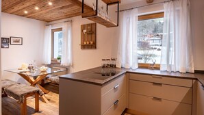 Moderni keittiö, jossa on puupalkkeja, lasinen ruokapöytä ja näkymä lumiseen maisemaan.