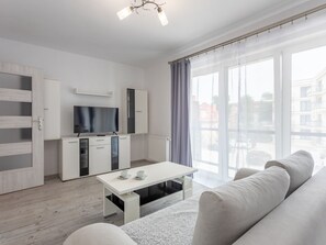 Ein modernes Wohnzimmer mit einer Couch, einem Couchtisch und einem Fernseher. Eine Glastür öffnet sich zu einem Balkon mit Blick auf die Stadt.