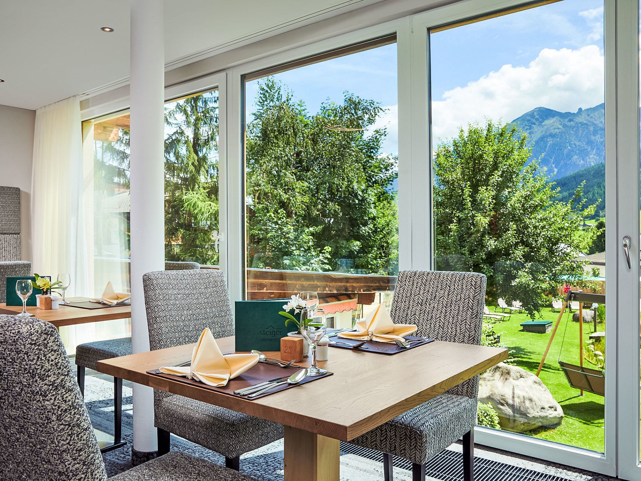 A dining area with a table set for two, large windows offering a view of a mountainous landscape.