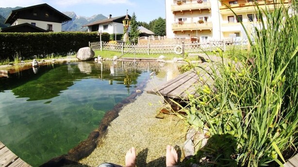 A clear pool with a wooden deck, surrounded by lush greenery and a mountain backdrop. - Wohnung Biohaus in Neukirchen am Großvenediger by Interhome (Neukirchen am Großvenediger)