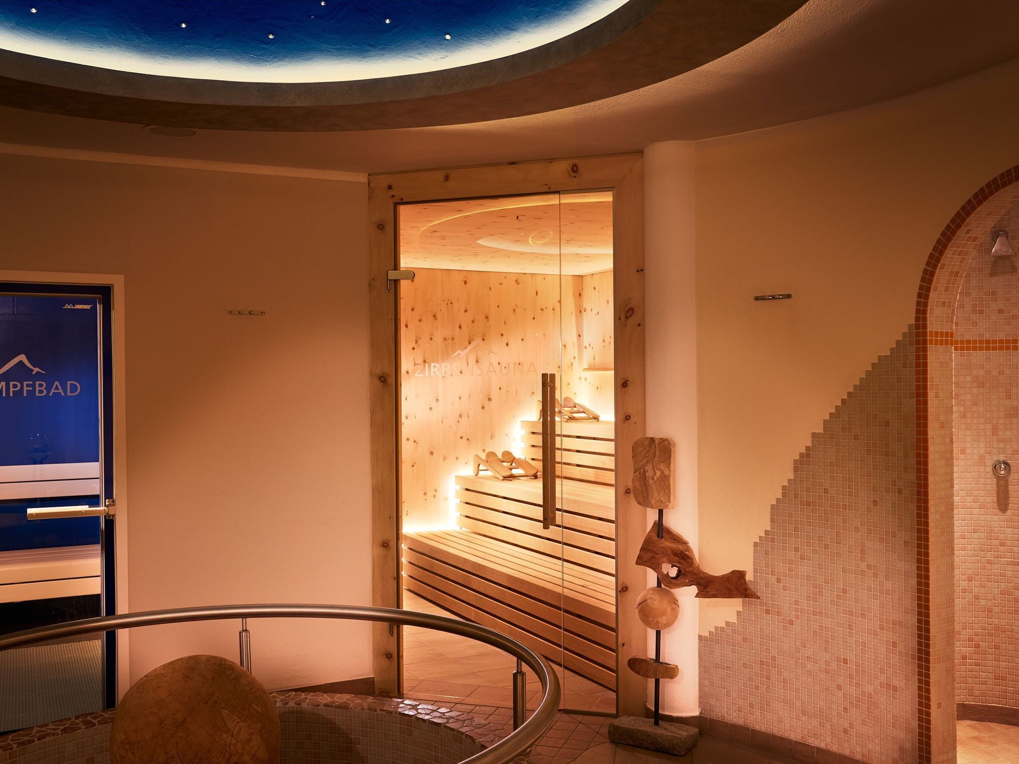 A hotel interior with a wooden staircase leading to a room with a wooden ceiling and a starry sky mural.