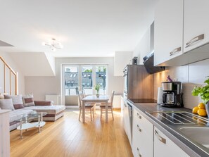 A modern kitchen with a built-in oven, a coffee maker, and a sink. There is a dining area with a table and chairs, and a sofa in the living room. - Helle Ferienwohnung Bianco 49 by Interhome (Swinoujscie)
