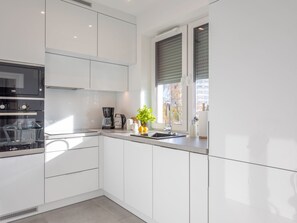 Una cucina moderna con mobili bianchi, un forno Bosch, una macchina per il caffè e una finestra con persiane.